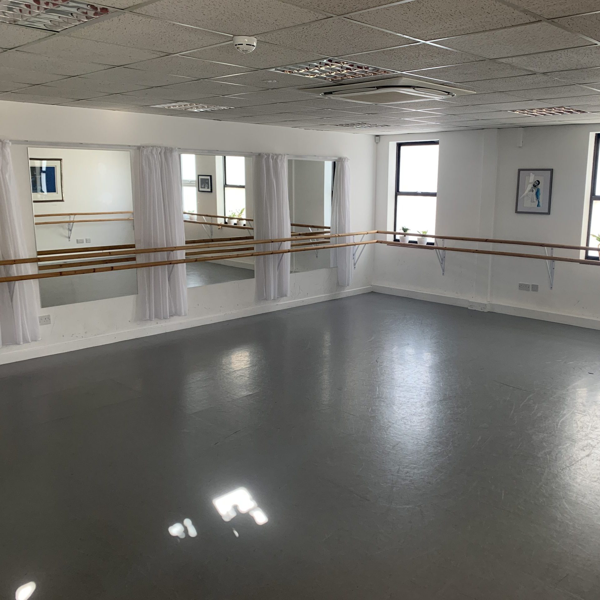 Dance studio with grey floor, mirrors on one wall and ballet barres along two walls